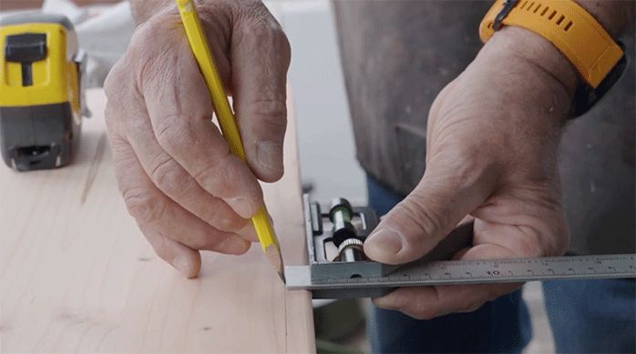 una persona marca un calado en el trozo de madera usando un lápiz y una regla.