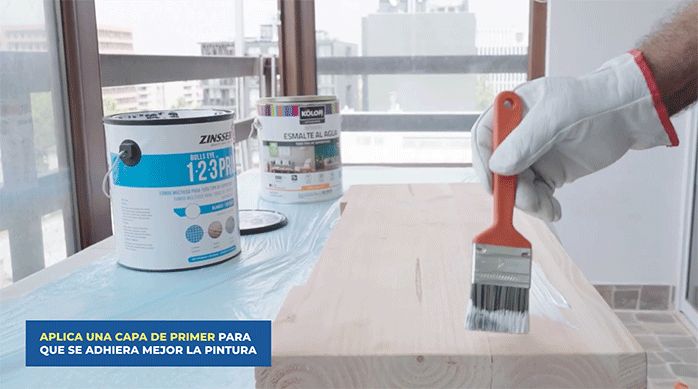 una persona aplica primer con una brocha en la cubierta de madera para hacer el tocador.