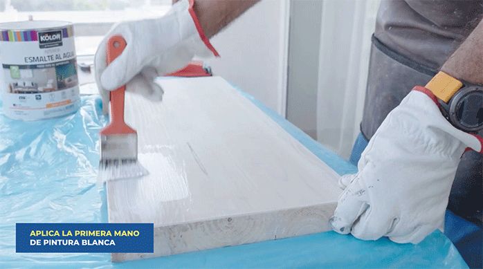 una persona aplica la primera mano de esmalte al agua blanco en la cubierta del tocador.