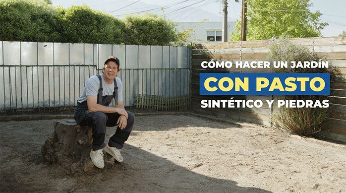 un hombre sentado en un árbol cortado, en un patio de tierra, listo para enseñar cómo hacer un jardín de pasto sintético y piedras.