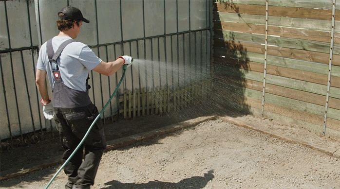 una persona moja el terreno con una manguera.