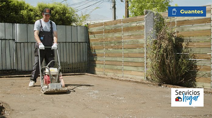 una persona pasa una placa compactadora por encima del patio en que hará el jardín de pasto sintético y piedras.