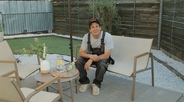 un hombre sentado en una terraza, en el nuevo jardín de pasto sintético y piedras.