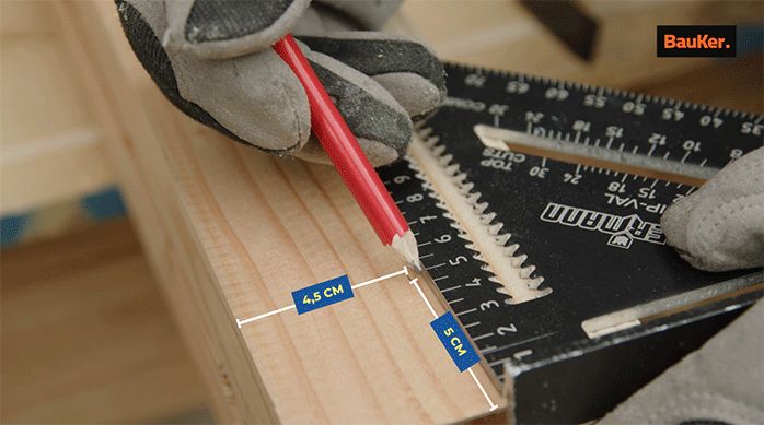una persona marca un trozo de madera al eje usando una escuadra y un lápiz.