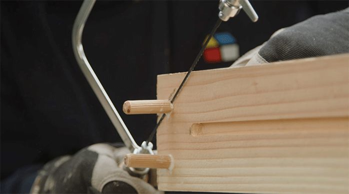 una persona corta los tarugos de madera usando una sierra manual.