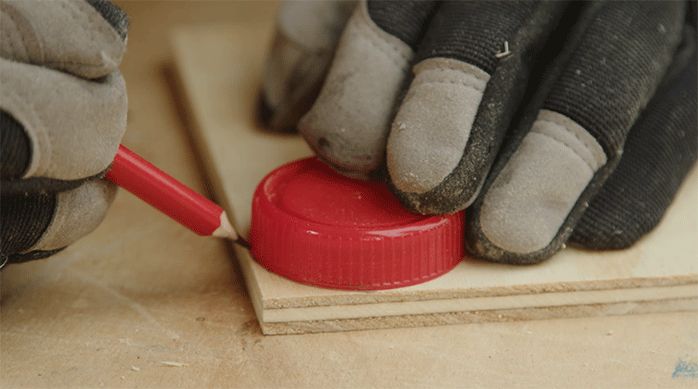 una persona usa una tapa para dibujar su contorno en la punta de un trozo de madera.