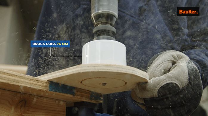 una persona usa una broca copa para cortar un círculo completo en un trozo de madera.