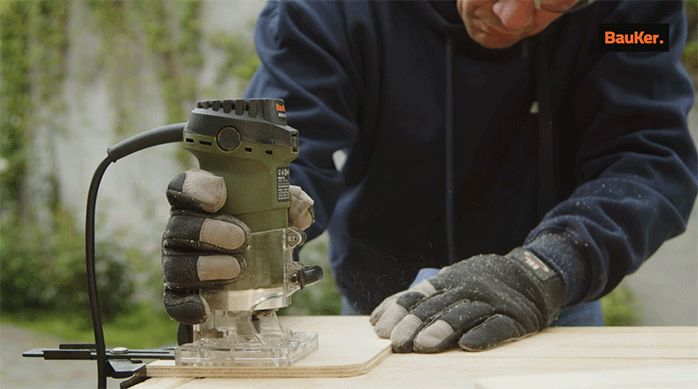 un hombre usa una fresadora para hacer unos calados en un trozo de madera.