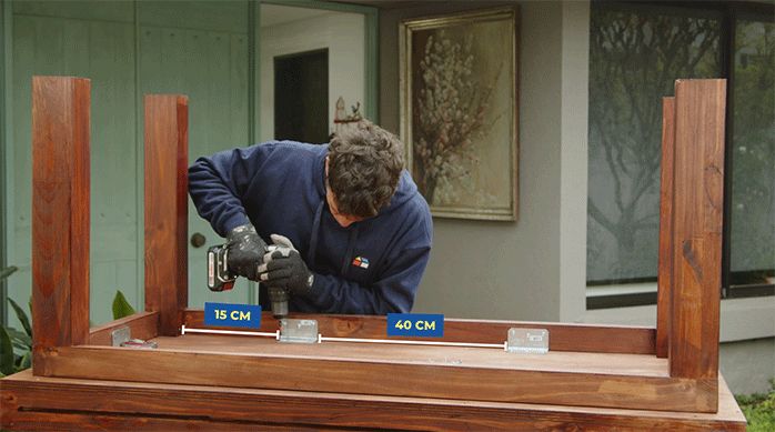un hombre fija la base a la mesa usando escuadras metálicas.
