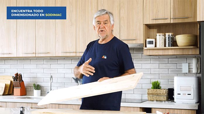 un hombre sostiene un trozo de pino finger, en una cocina de tonos neutros.