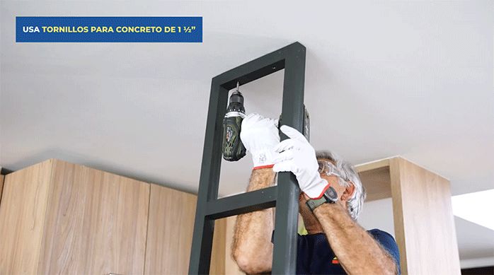 un hombre fija uno de los soportes de la repisa colgante al cielo de la cocina.