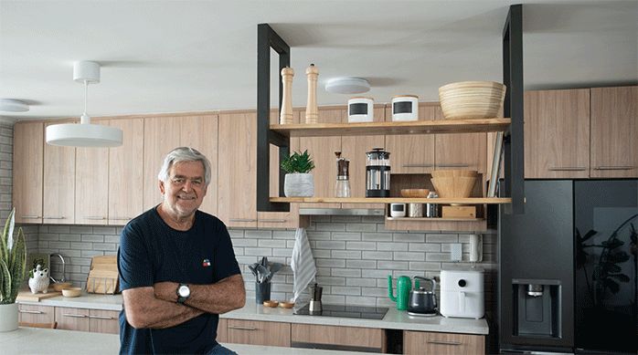 un hombre apoyado en el mesón de una cocina, junto a la repisa colgante de madera recién terminada.