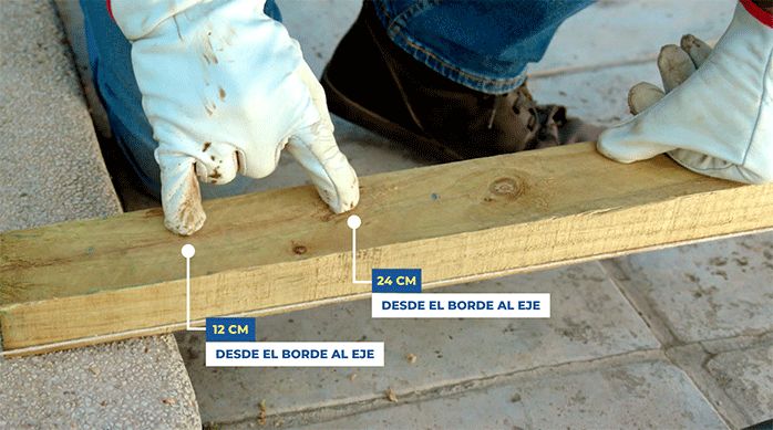 una persona indica los lugares de perforación del trozo de pino, que son a 12 y 24 cm desde uno de sus extremos.