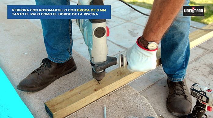una persona presenta y perfora a través del palo de pino en el borde de cemento de la piscina.