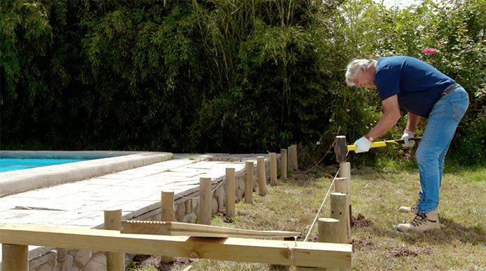 un hombre entierra un polín de la segunda hilera de polines de la base del deck de madera.
