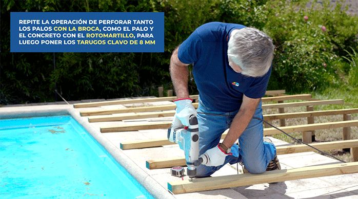 un hombre perfora a través del palo de madera hacia el cemento del borde de la piscina usando un rotomartillo.