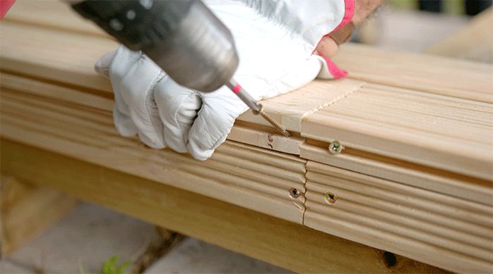 una persona fija la primera tabla del deck de madera con un tornillo en el borde.