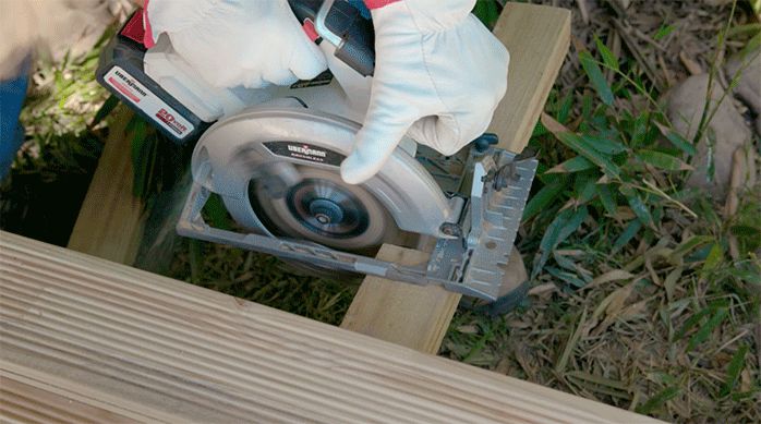 una persona corta el excedente de los bordes del deck de madera para piscina usando una sierra circular.