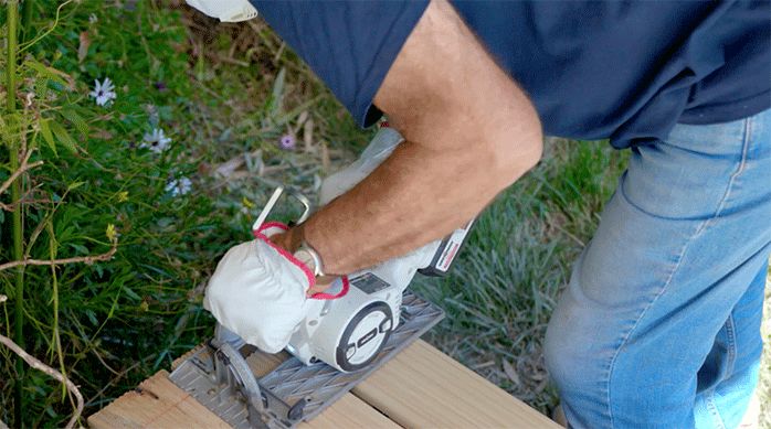 una persona corta el excedente de los bordes del deck de madera para piscina usando una sierra circular.
