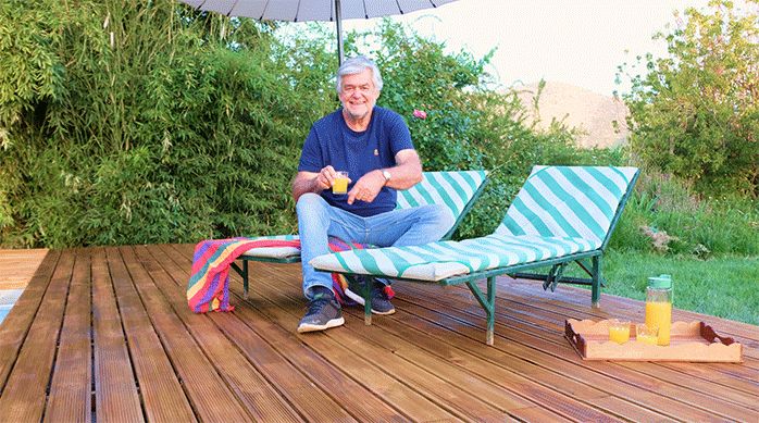 un hombre sentado en una reposera, sobre un deck de madera para piscina recién terminado.