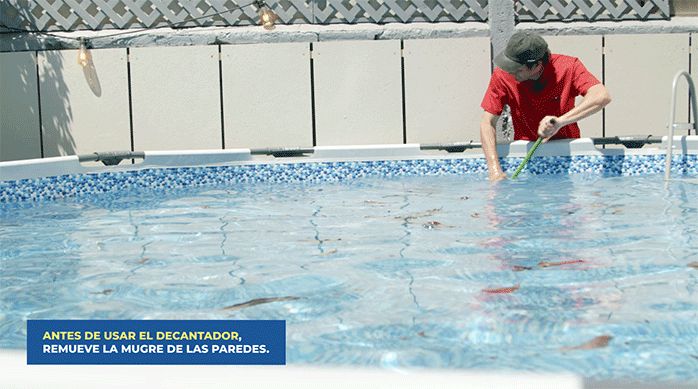 un hombre usa un escobillón para remover la mugre pegada en las paredes de una piscina.