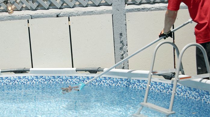 un hombre usa una malla para limpiar la superficie del agua de la piscina.