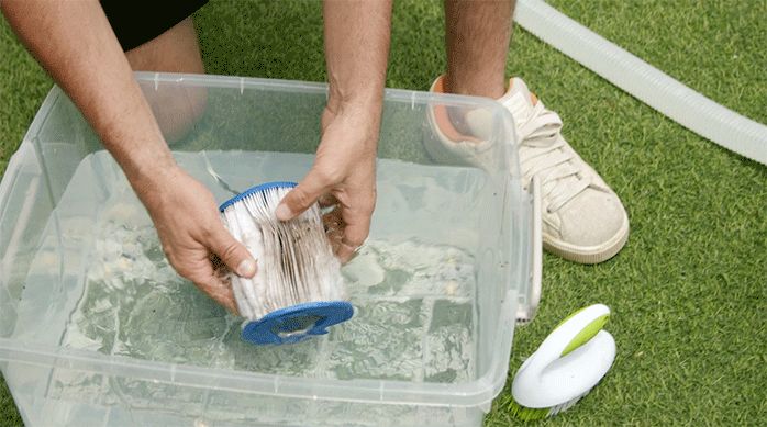 un hombre limpia un filtro de piscina en una recipiente con agua limpia.