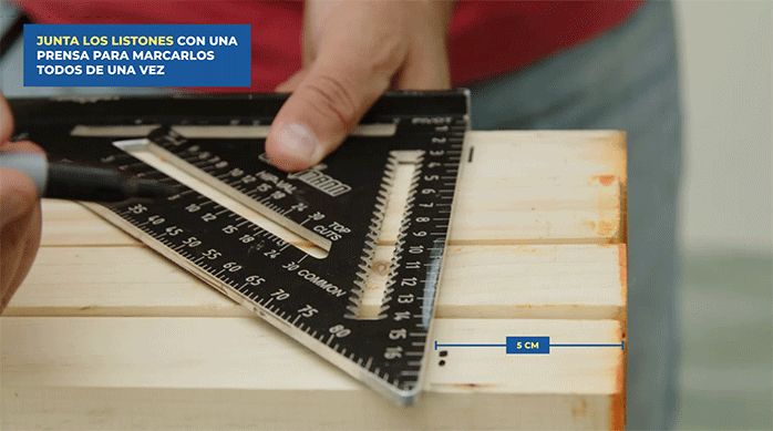 un hombre marca los listones de pino seco cepillado a 5 cm desde los extremos usando una escuadra y un lápiz.