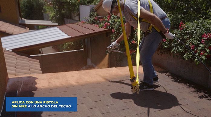 un hombre pinta un techo de tejas asfálticas con un sellador para techos coolguard, usando una pistola para pintar sin aire.