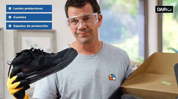 un hombre con lentes de seguridad sostiene unos zapatos con suela de goma.