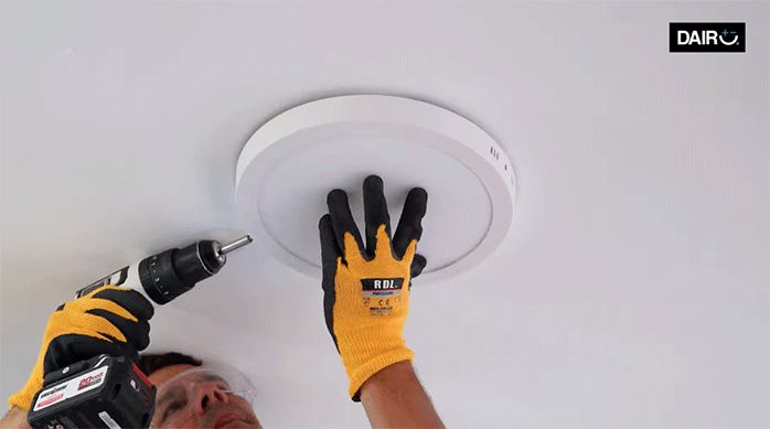 un hombre instala el panel led en su soporte, en el cielo raso de una habitación.