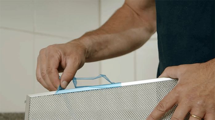 una persona retira los protectores plásticos de las rejillas de la campana de extracción.