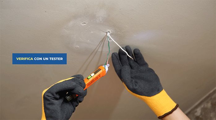 una persona con guantes de seguridad usa un tester para asegurarse de que la electricidad está cortada en unos cables.