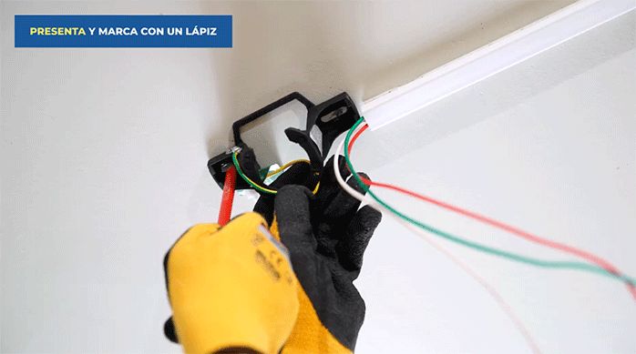 un hombre presenta el soporte del ventilador de techo y marca las perforaciones a través de sus agujeros.