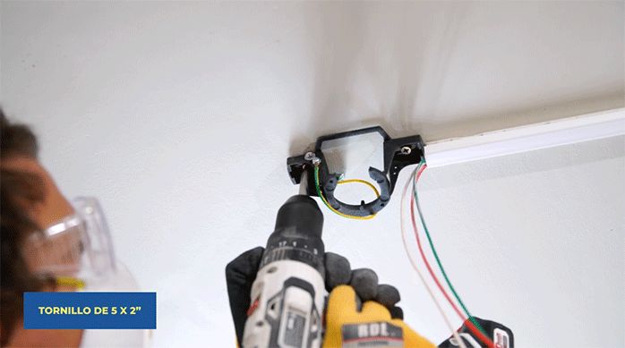 un hombre atornilla el soporte del ventilador de techo.