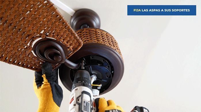 un hombre fija un aspa del ventilador al motor del ventilador de techo.