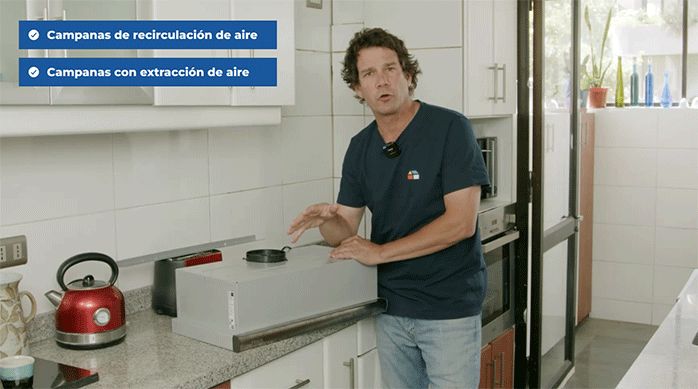 un hombre en una cocina con una campana de extracción apoyada en el mesón.
