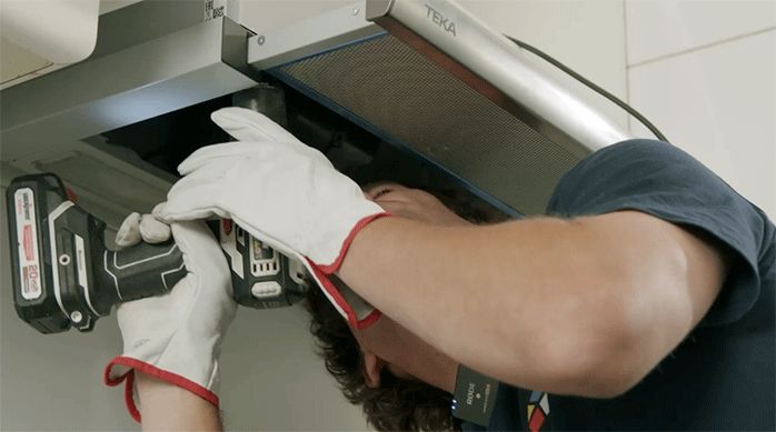 un hombre fija la campana de extracción al mueble de melamina.