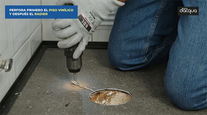 un hombre perfora el piso vinílico del baño con una broca punta flecha.