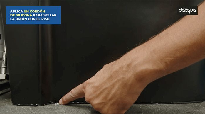 una persona pasa el dedo húmedo por el cordón de silicona negra que aplicó en la junta entre el sanitario y el piso vinílico.