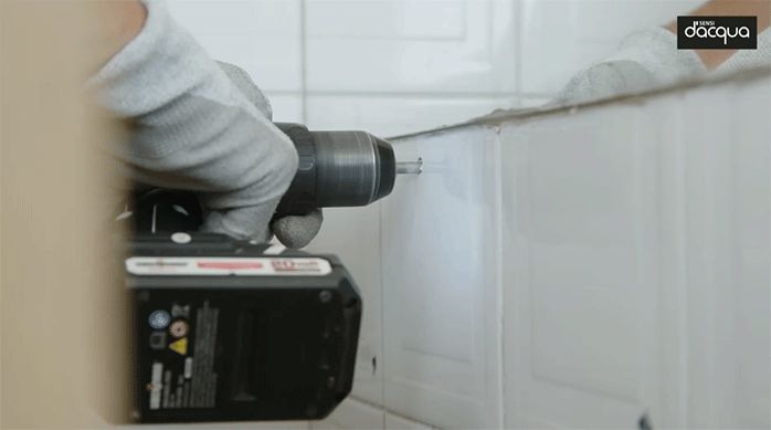 una persona perfora el muro de cerámica del baño para instalar el vanitorio.