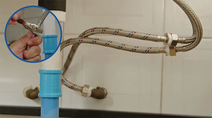 una persona conecta los flexibles del monomando del lavamanos a las conexiones de agua del baño.