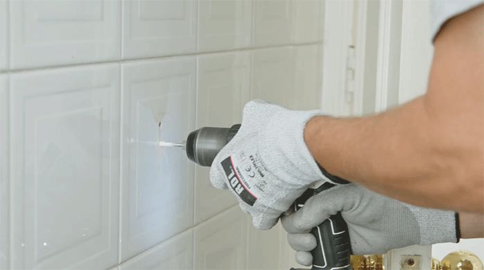 una persona perfora el muro de un baño para instalar los accesorios de color negro mate.