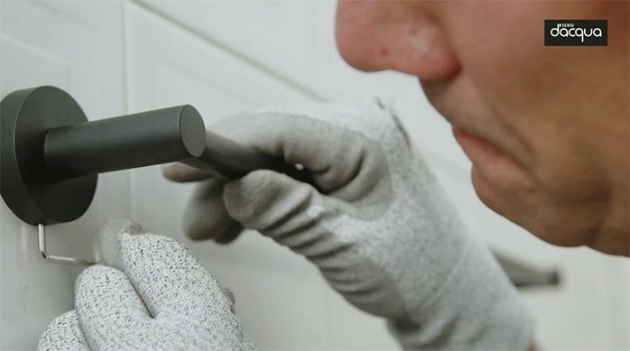 una persona usa una llave allen para fija el toallero de color negro mate en el muro del baño.