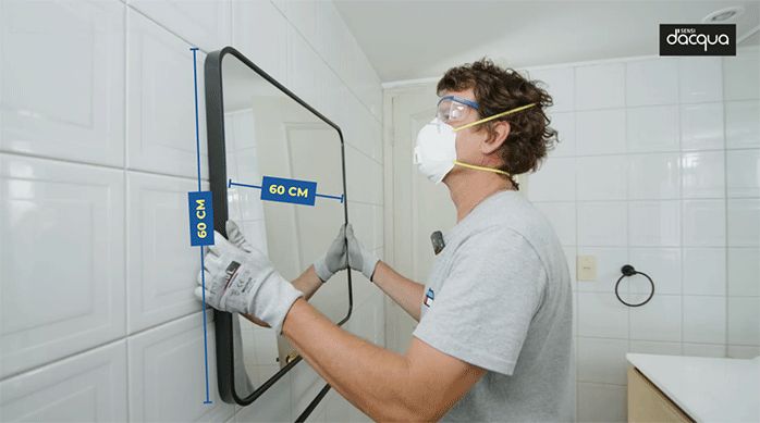un hombre instala un vidrio rectangular en la pared posterior del baño.