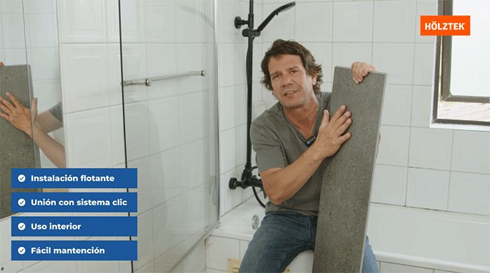 un hombre sostiene una plancha de piso vinílico holztek en un baño que está a punto de remodelar.