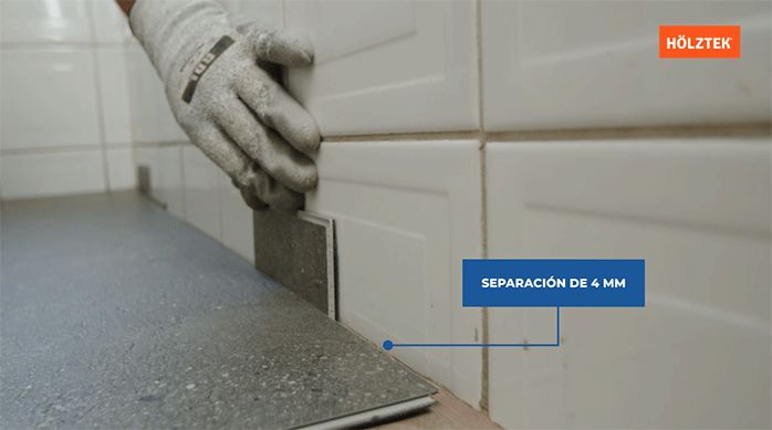 una persona usa un trozo de piso vinílico para calcular la distancia entre el muro y las planchas de piso vinílico.