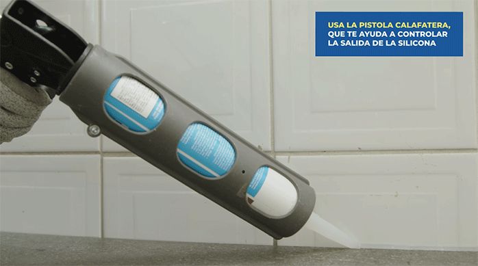 una persona aplica un cordón de silicona en la juntura del piso vinílico con el muro usando una pistola calafatera.