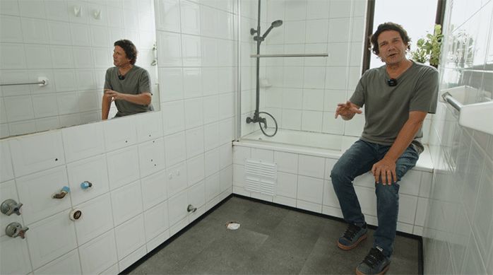 un hombre sentado en el borde de una tina en un baño recién remodelado con piso vinílico.