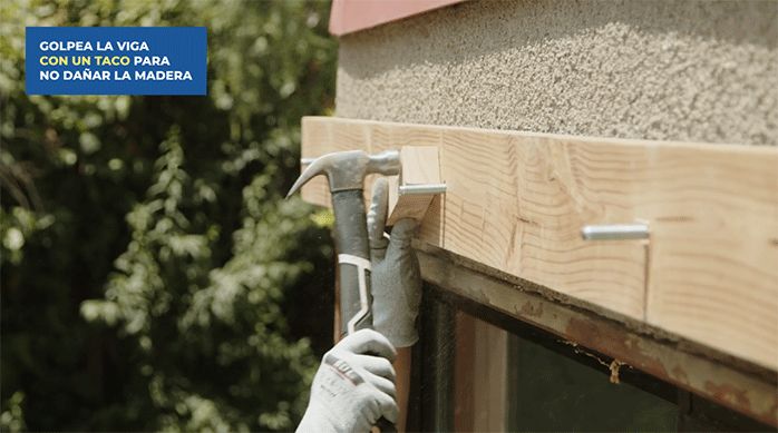 una persona golpea la viga principal usando un martillo y un taco de madera.